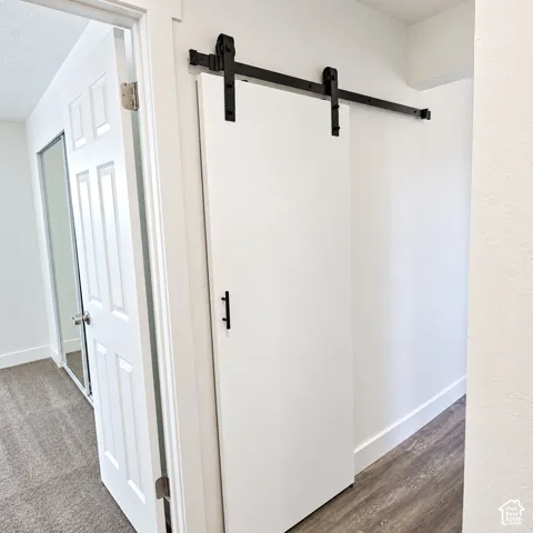 White sliding barn door featuring matte black hardware, vertical handle, wood-finish flooring, and a six-panel hinged door