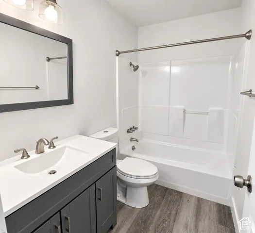 Updated bathroom featuring a charcoal vanity with a white countertop, integrated sink, brushed metal fixtures, and wood-finish flooring