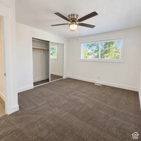 Neutral-toned carpeting, ceiling fan with integrated light fixture, and closet with sliding mirrored doors