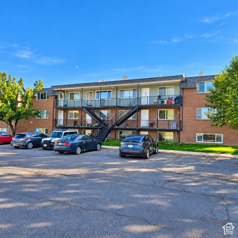 Multi-story brick exterior featuring black metal staircases and balcony railings with asphalt parking area