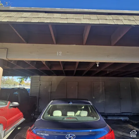 Covered parking structure featuring shingle roofing, exposed timber rafters, and four secure storage access doors