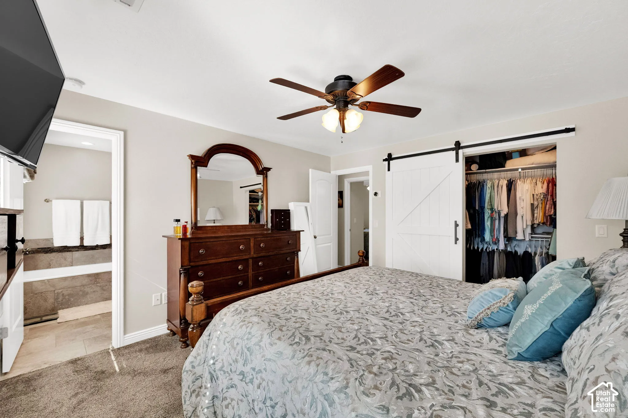 Bedroom interior featuring neutral wall paint, carpeting, a ceiling fan with integrated lighting, and a closet with a white sliding barn door