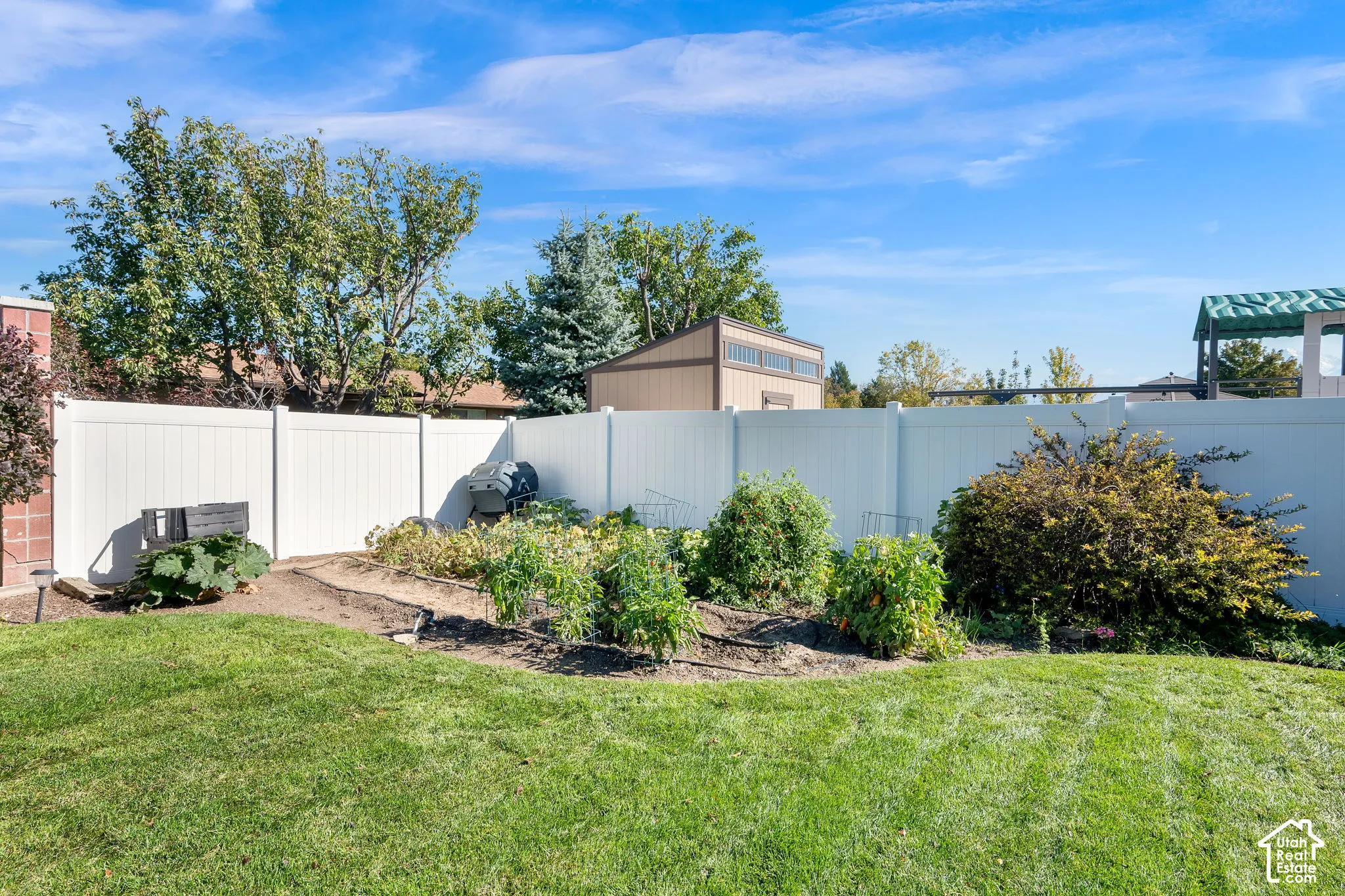 Backyard featuring a manicured lawn, established garden beds, full-height vinyl fencing, and a detached storage structure