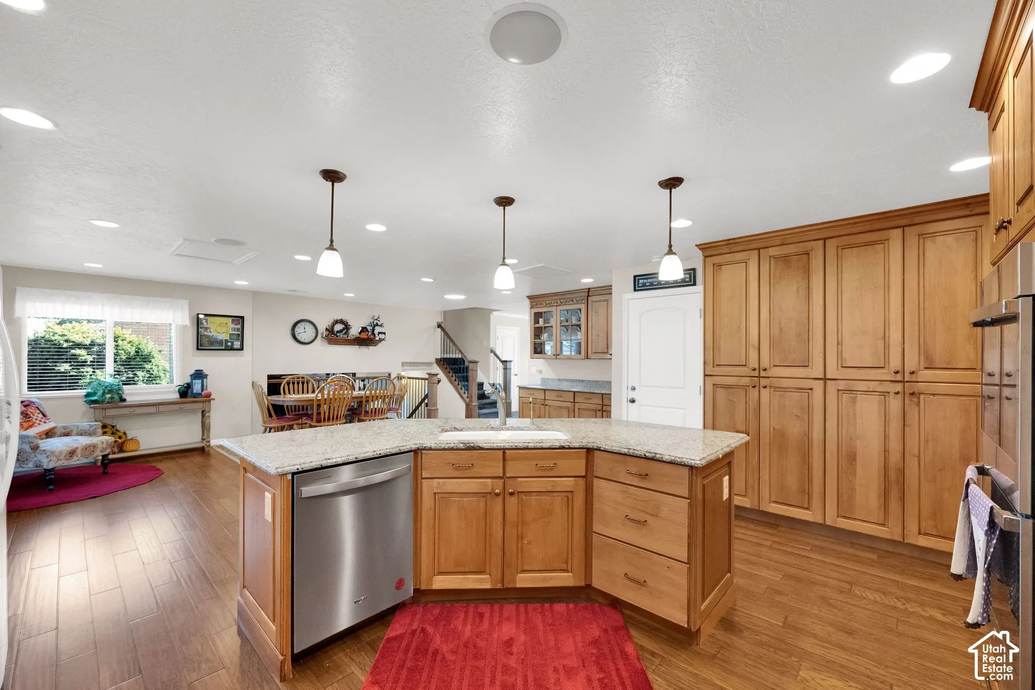 Kitchen featuring natural-finish wood cabinetry, a central island with stone-surface countertop and integrated dishwasher, wood-finish flooring, and recessed lighting