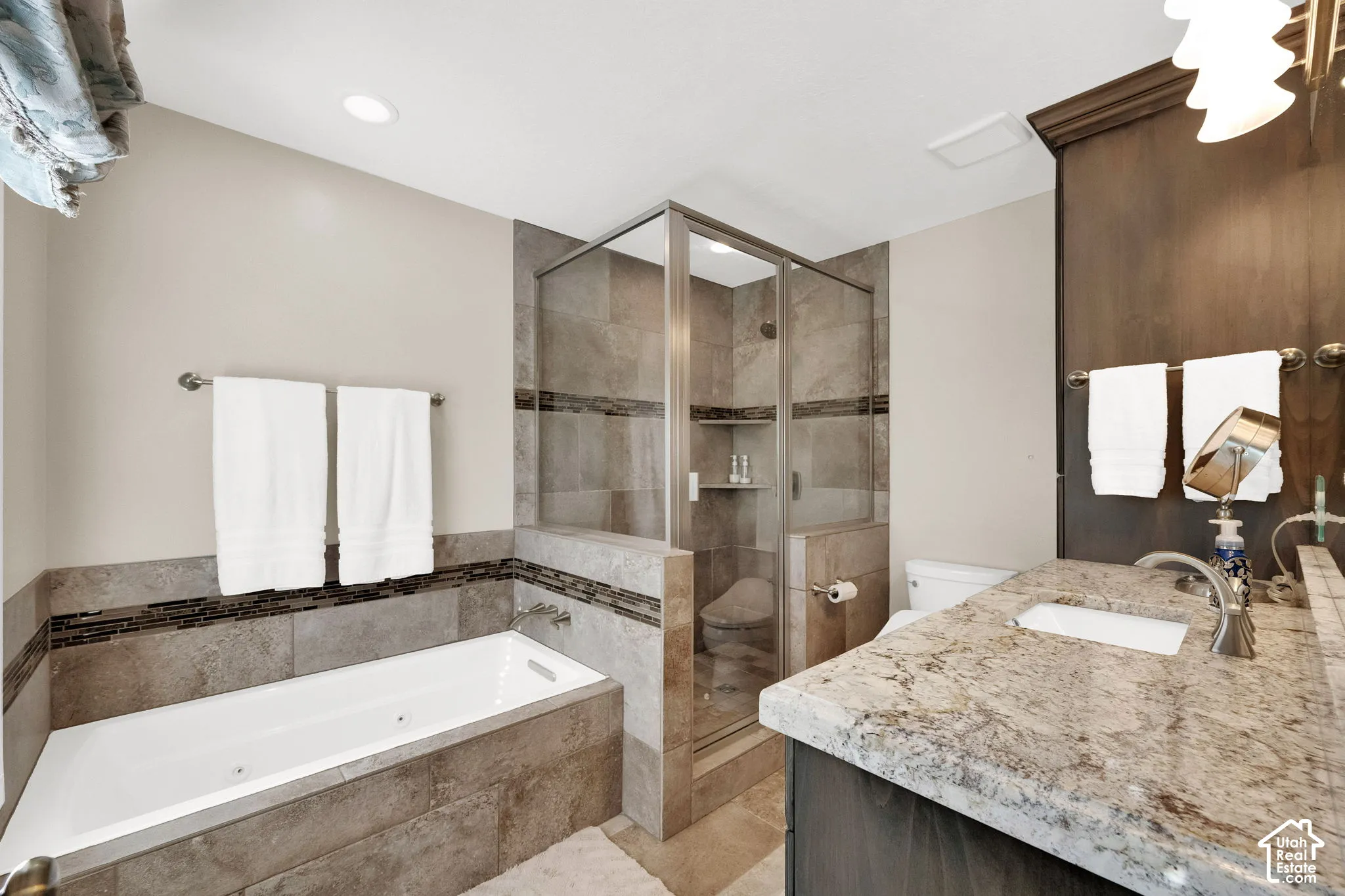 Deep soaking tub and separate glass-enclosed shower with tile surround, natural stone countertop, and dark wood-finish cabinetry