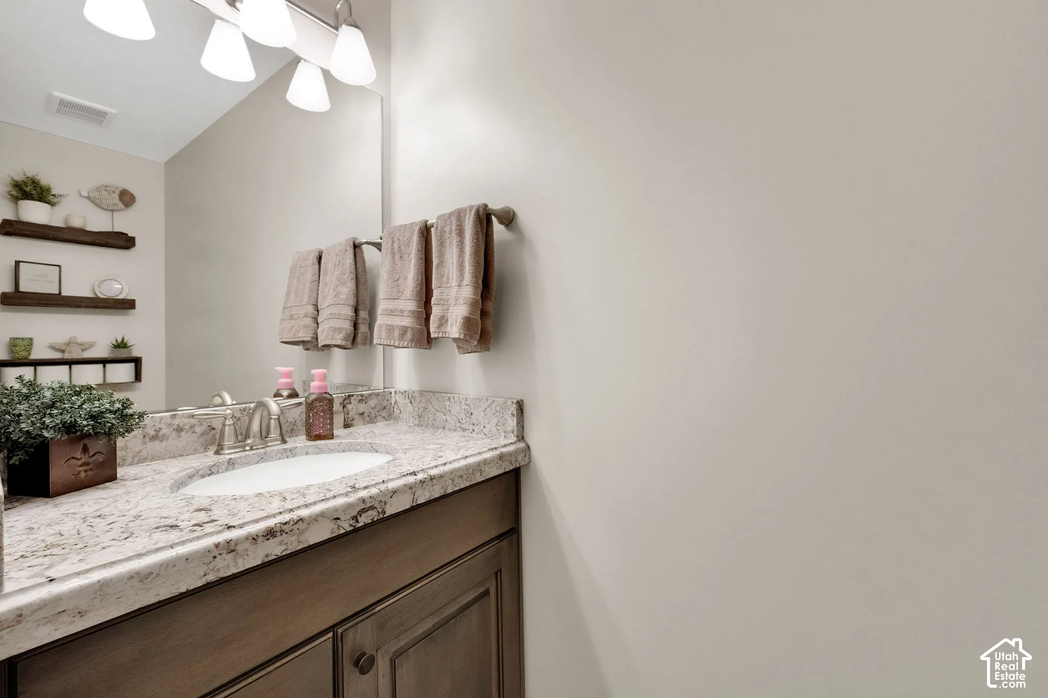 Bathroom vanity with stone-finish countertop, undermount sink, multi-drawer cabinetry, wall-mounted light fixture, and floating shelving