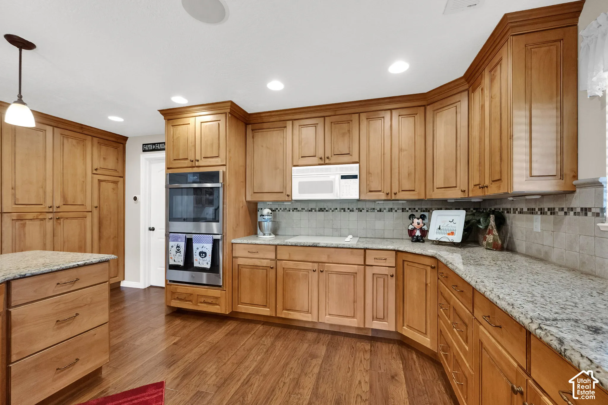 Kitchen featuring wood cabinetry, stone countertops, integrated stainless steel double oven, tile backsplash, and wood-finish flooring