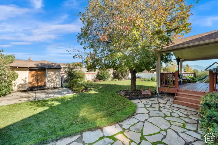 Backyard featuring an expansive lawn, flagstone patio, covered wood deck with stairs, and a detached storage structure
