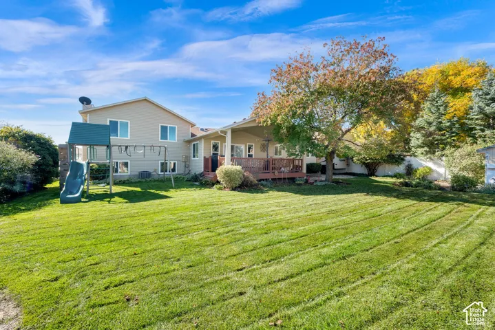 Expansive backyard featuring a sprawling lawn, mature trees, a raised wood deck, and a structure for recreational activity