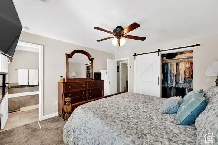 Bedroom interior featuring neutral wall paint, carpeting, a ceiling fan with integrated lighting, and a closet with a white sliding barn door
