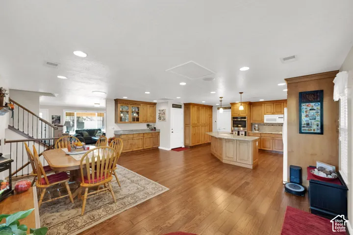 Kitchen featuring wood cabinetry, an expansive central island, recessed lighting, and wood-finish flooring