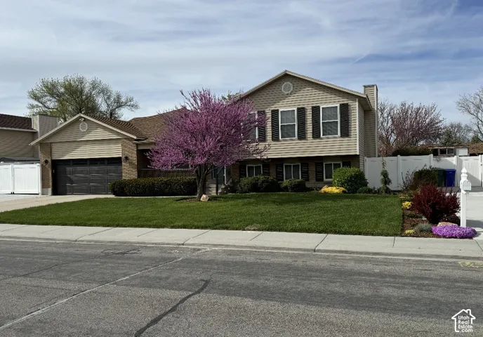 Split-level exterior featuring vinyl siding, dark shutters, an attached two-car garage, and white vinyl perimeter fencing