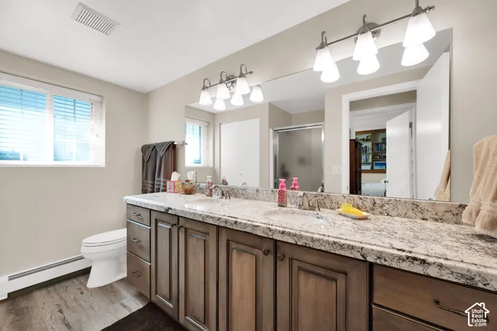 Dual-sink vanity featuring stone-finish countertops, wood-toned cabinetry, full-width vanity mirror, and dual multi-bulb light fixtures