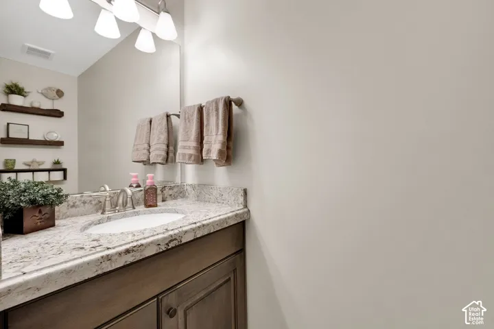 Bathroom vanity with stone-finish countertop, undermount sink, multi-drawer cabinetry, wall-mounted light fixture, and floating shelving