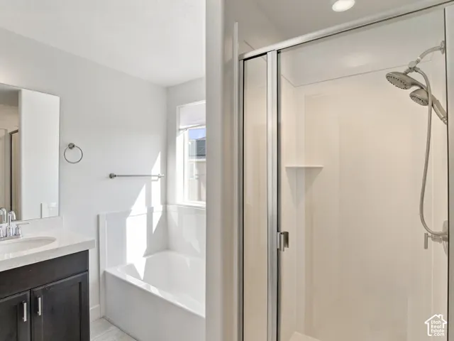 Bathroom featuring a vanity with a white countertop, a built-in soaking tub with a tiled surround, and a walk-in shower with a glass door enclosure and a dual-head shower fixture