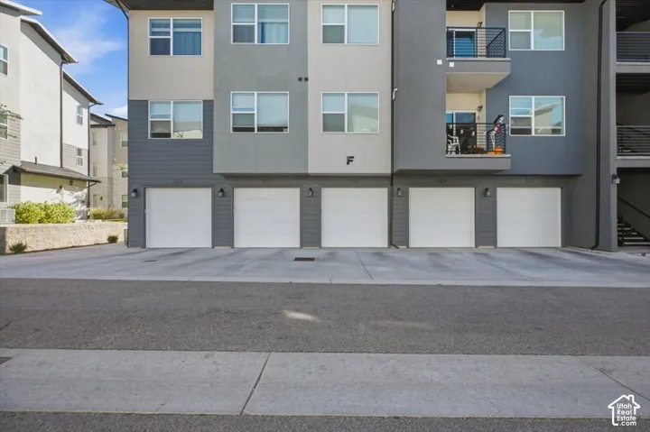 Modern multi-story exterior featuring a mix of grey and neutral stucco siding, private balconies with metal railings, and integrated multi-car garage access