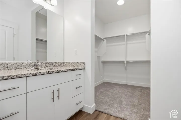 Bathroom vanity featuring white cabinetry, stone-finish countertop, undermount sink, and full-width mirror, paired with a carpeted walk-in closet featuring metal shelving