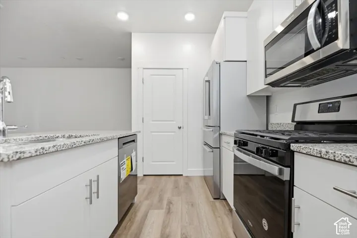 Kitchen featuring white cabinetry, stone-surface countertops, wood-finish flooring, and stainless steel appliances