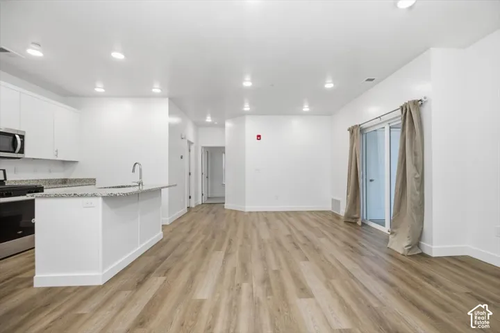 Open-concept interior featuring wood-finish flooring, white cabinetry, stone-finish countertops, recessed lighting, and a sliding glass door