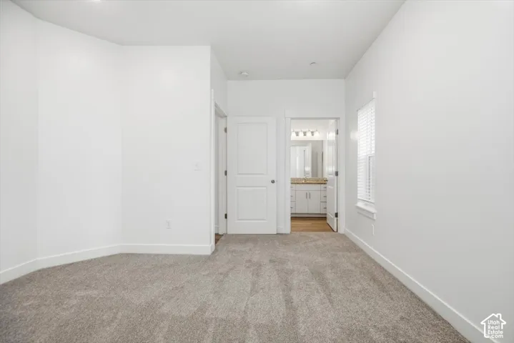 Neutral-toned carpeting, crisp white wall finish, single-panel interior door, and window with built-in blinds