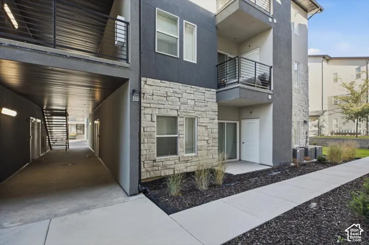Multi-story exterior featuring a stone veneer facade, stucco siding, a private balcony with horizontal metal railings, and a covered ground-level entry area