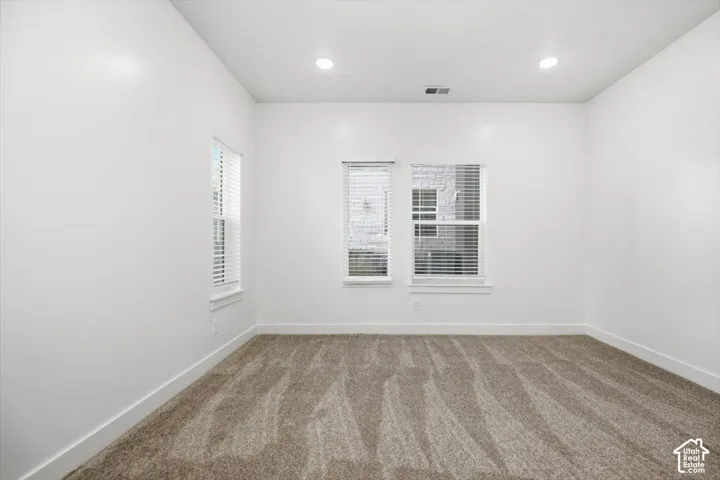 Neutral interior room featuring neutral-tone carpeting, smooth walls, recessed lighting, and windows equipped with horizontal blinds