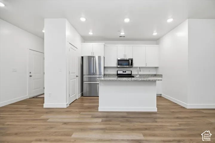 Kitchen featuring white cabinetry, stone-surface countertops, stainless steel appliances, a center island, and wood-finish flooring