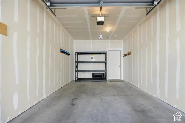 Attached garage featuring concrete flooring, drywall finish, ceiling-mounted automatic door opener, and mounted wall storage racks
