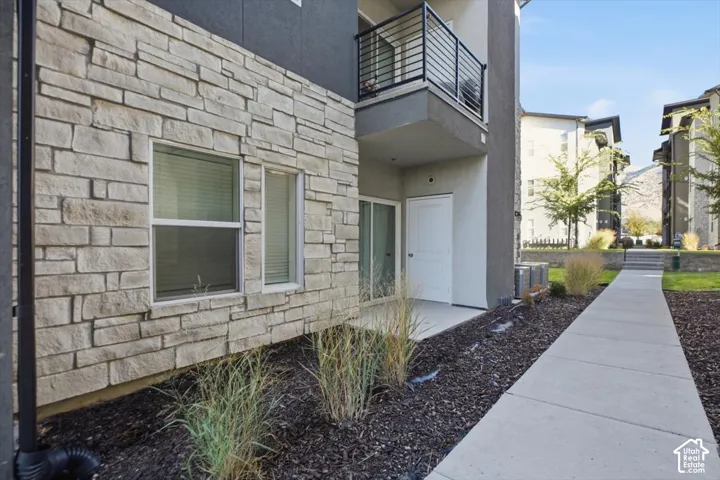 Exterior facade featuring stone veneer masonry, dark-toned stucco, a balcony with a black metal railing, and a concrete pathway