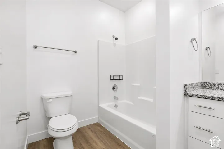 Bathroom featuring wood-finish flooring, white vanity with stone-style countertop, integrated shower and tub surround, and polished metal hardware