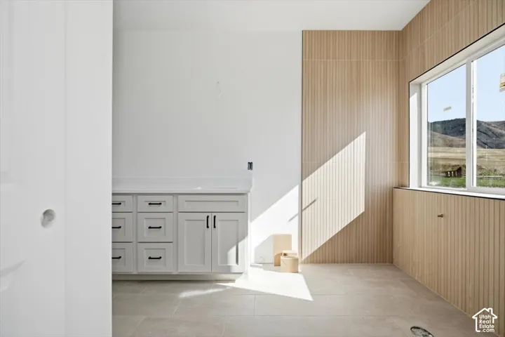 Bathroom featuring light gray shaker-style cabinetry, white countertop, large-format tile flooring, vertical wood-finish wall paneling, and mountain scenery through the window