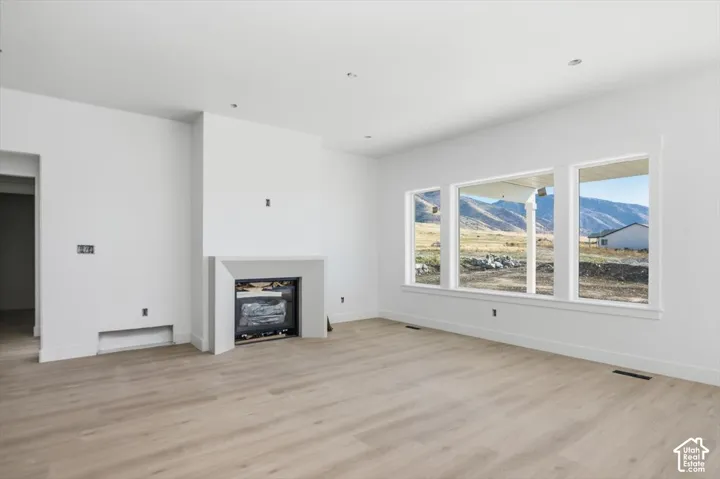 Living area featuring wood-finish flooring, a minimalist fireplace surround, recessed lighting, and expansive windows showcasing a mountain backdrop