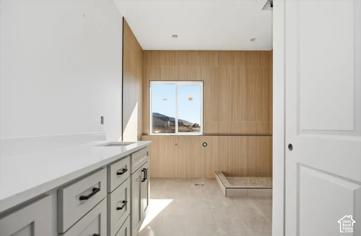 Bathroom featuring wood-finish wall tile, a stone-composite countertop, light gray cabinetry with matte black hardware, recessed ceiling lighting, and tile flooring
