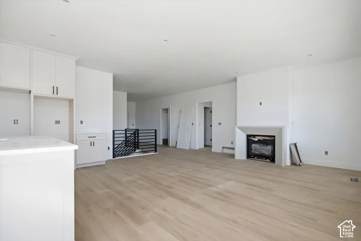 Open-concept interior featuring light wood-finish flooring, custom white cabinetry, a fireplace with a geometric stone surround, recessed lighting, and a black metal stair railing