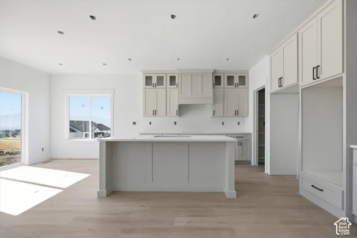 Kitchen featuring custom cabinetry with glass-paneled upper doors, a central island with a stone countertop, wood-finish flooring, and recessed lighting