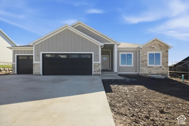 Single-story exterior featuring vertical siding, stone masonry accents, a three-car garage, and a concrete driveway