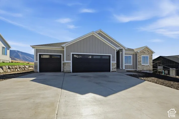 Exterior featuring vertical siding, stone veneer accents, a three-car garage, and a concrete driveway, set against a mountain backdrop