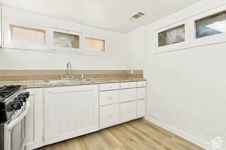 Kitchen featuring stone-finish countertops, tile backsplash, white cabinetry, wood-finish flooring, and high-set horizontal windows