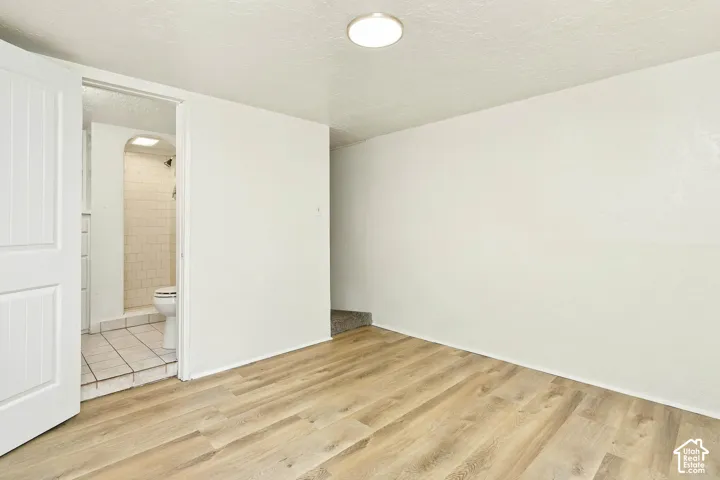 Room featuring wood-finish flooring, white walls, and a flush-mount light fixture, with entry to a tiled bathroom containing a walk-in shower