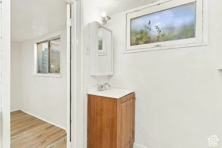 Wood-finish cabinetry vanity with white countertop, integrated sink, and chrome faucet, accompanied by a wall-mounted medicine cabinet and horizontal windows