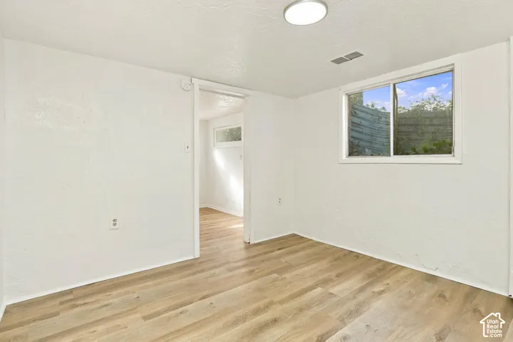 Room with wood-finish flooring, white walls, and a sliding window featuring an exterior window well