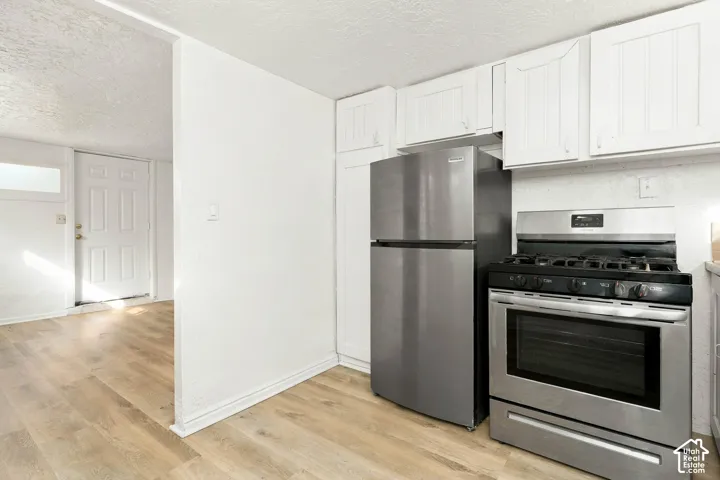 Kitchen featuring white cabinetry, stainless steel refrigerator, stainless steel gas range, and wood-finish flooring