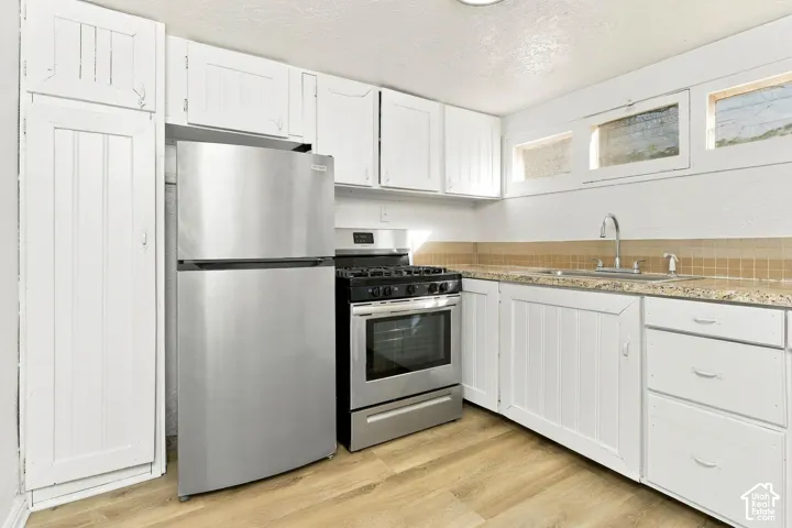 Kitchen featuring white vertical-panel cabinetry, wood-finish flooring, stainless steel appliances, stone-look countertops, and horizontal clerestory windows