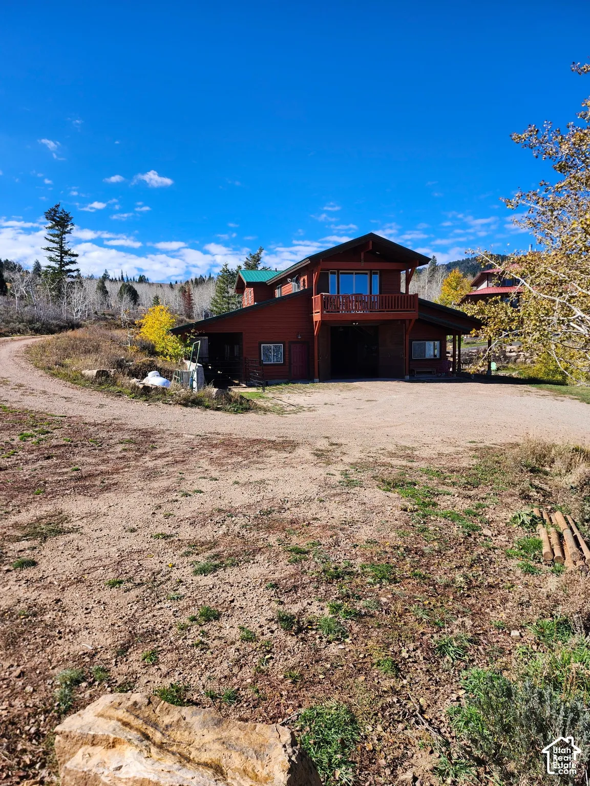 Red wood-sided exterior featuring an elevated balcony, a metal roof, and a gravel driveway