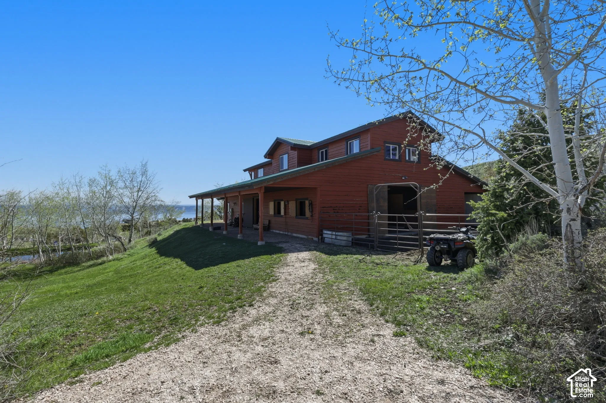 Red wood-sided exterior featuring an expansive covered porch, metal roofing, integrated horse stalls, and a gravel driveway