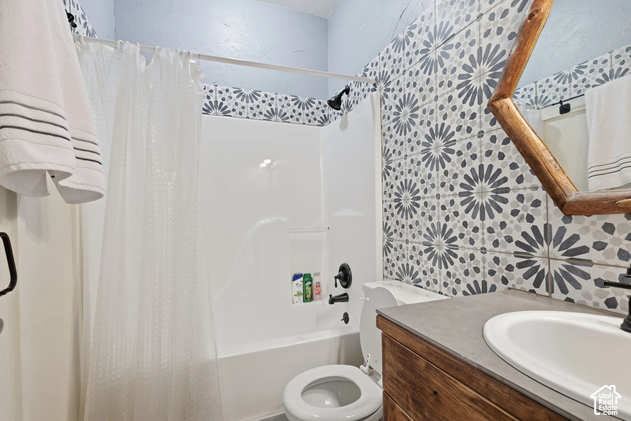 Bathroom featuring patterned wall tile, vanity with wood-finish cabinetry, neutral countertop, and matte black plumbing fixtures
