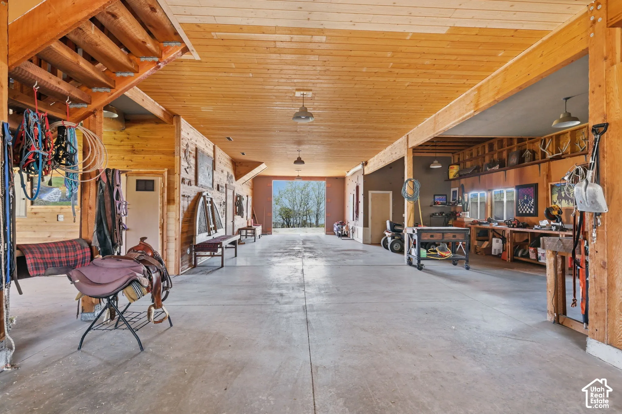 Expansive outbuilding featuring exposed wood-beam construction, tongue-and-groove wood ceilings, concrete flooring, built-in wooden shelving, and industrial-style pendant lighting