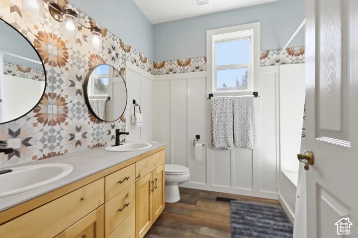 Bathroom featuring a wood-finish vanity with dual undermount sinks, patterned tile backsplash, board and batten wainscoting, and circular wall-mounted mirrors