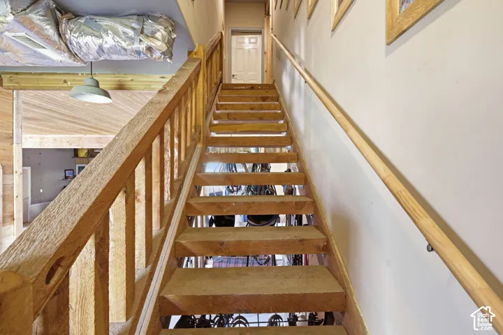 Open-riser staircase featuring natural wood construction, vertical wood balusters, and a wall-mounted wooden handrail