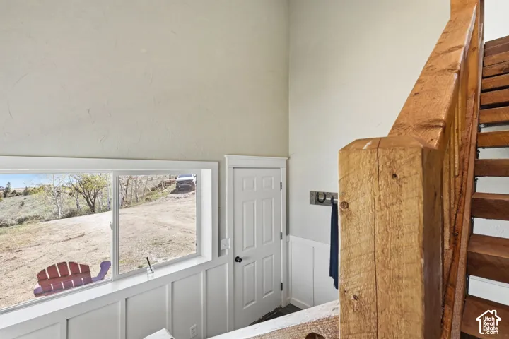 Staircase with custom rough-hewn timber handrail and treads, white wainscoting, vaulted ceiling, and expansive horizontal window